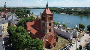 a tall building with a steeple on the side of a river at Sercowe Zacisze in Chełmża