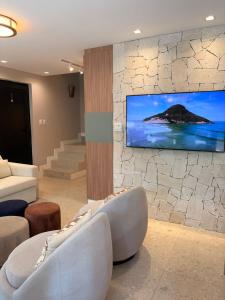 a living room with a tv on a stone wall at Refúgio com Pé na Areia in Mata de Sao Joao