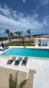 a swimming pool with two lounge chairs and palm trees at maison rachid in El Guecheïne
