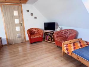 a bedroom with a bed and two chairs and a television at Zacisze pod lasem in Ruciane-Nida