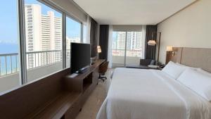 a hotel room with a bed and a tv and windows at Holiday Inn Acapulco Amarea by IHG in Acapulco
