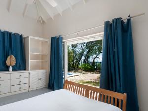 a bedroom with a bed and a window with blue curtains at Stunning Views Oceanfront Oasis with Private Pool - Inch by Inch in Christ Church +21 photos