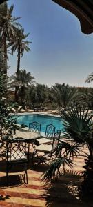 a table and chairs next to a pool with palm trees at Riad Kasbah Le Touareg in Merzouga