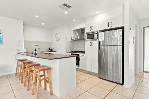 a kitchen with white cabinets and a refrigerator and stools at Coast Bliss on Currambene in Huskisson
