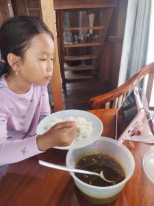 a little girl sitting at a table eating rice at Selambak View Cottage in Pulau Siantan