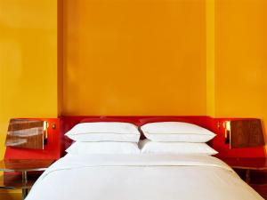a bed with four pillows against a yellow wall at The Manner, The Unbound Collection by Hyatt in New York