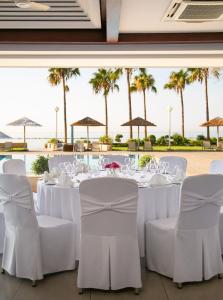 a dining room with white tables and chairs and palm trees at Atlantica Miramare Beach in Limassol