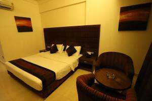 a hotel room with a bed and a chair at Hotel Kohinoor, Bharuch in Bharūch +4 photos