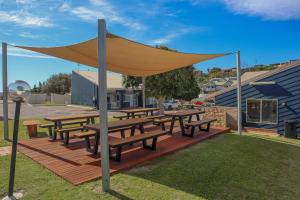 Eine Gruppe von Picknicktischen mit einem Sonnensegel auf einer Terrasse in der Unterkunft Waves Geraldton in Geraldton