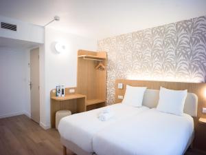a bedroom with a white bed and a wall at BRIT HOTEL CONFORT Roissy Saint-Witz in Saint-Witz