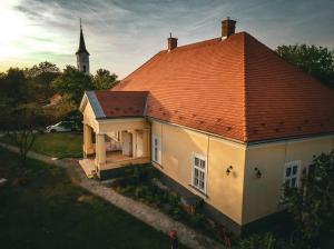 a white house with an orange roof and a church at Dinnyés Kúria Dabas in Dabas