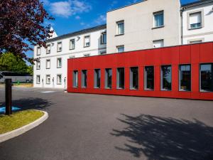a building with a red wall in a parking lot at BRIT HOTEL CONFORT Roissy Saint-Witz in Saint-Witz