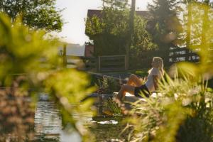 a woman sitting on a ledge next to a pond at Bergchalet mit Wellness-Oase, Natur Pur in Pöllauberg