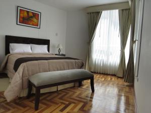 um quarto com uma cama, um banco e uma janela em Apartamentos Quewe em Cusco