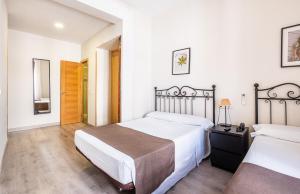 two beds in a bedroom with white walls and wooden floors at Hostal El Pilar in Madrid