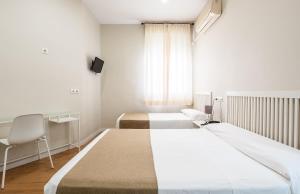 a hotel room with two beds and a chair at Hostal El Pilar in Madrid