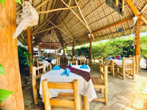a restaurant with tables and chairs and a straw roof at Balungi Boutique Hotel in Uroa