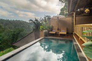 a swimming pool with two chairs and an umbrella at The Compass Rose Valley in Ubud