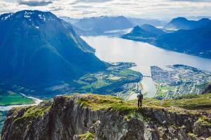 a man standing on top of a mountain overlooking a lake at Frichs Ekspress Åndalsnes in Åndalsnes