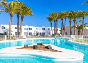 a large swimming pool with palm trees in the background at Los Barqueros Suites Palm in Corralejo +3 photos