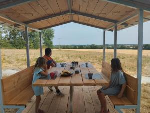 a man and two girls sitting at a picnic table under a roof at La Grande Grange 89 in Saint-Martin-des-Champs