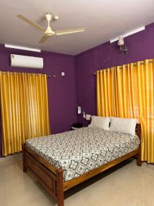 a bedroom with a bed with yellow curtains and a ceiling fan at Mud apples stay in Varkala