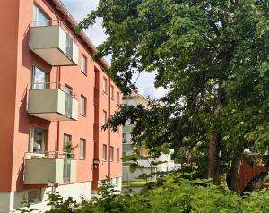 a red building with a balcony and a tree at Prinshöjden Apartments - Katrineholm Central in Katrineholm