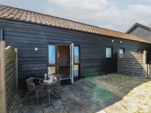 a black house with a patio and a table at Snowy Owl Barn in Shipdham