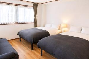 two beds in a room with a couch and a window at Tokyo Grand House in Akishima