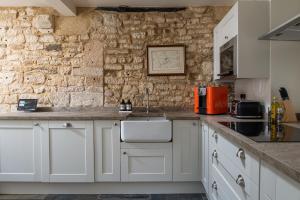 a kitchen with white cabinets and a stone wall at Tranquility House in Painswick +19 photos