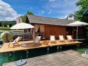 a deck with chairs and umbrellas on the water at Villa Gabriela Boutique Pension in Pörtschach in Pörtschach am Wörthersee