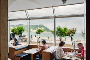 a group of people sitting at tables in a restaurant with a large window at Hotel Niza in San Sebastián