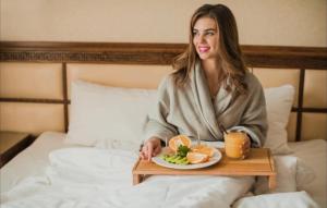 Eine Frau sitzt mit einem Tablett voller Essen auf einem Bett. in der Unterkunft Tejaji हाउसिंग in Jodhpur + 16 Fotos