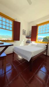 a bedroom with a bed and a table and windows at Pousada Café e Prosa Centro Histórico Paraty in Paraty