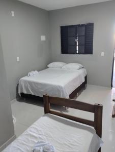 two beds in a white room with a window at Pousada e Restaurante Jacuba in Arealva