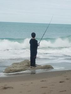 a man standing on the beach holding a fishing rod at Arena & mar in Las Grutas