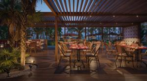 a restaurant with tables and chairs and palm trees at JOIA Rose Hall by Iberostar - Adults Only All Inclusive Resort in Montego Bay