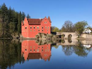 a large red castle sitting on top of a lake at Chalupa Na konci Lhoty in Pluhův Žďár