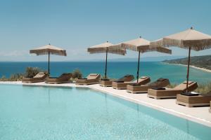 a swimming pool with chairs and umbrellas and the ocean at Manas Villas in Elaiokhórion