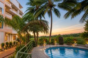 a resort swimming pool with palm trees and a building at Home Stay CampoDeVista in Calangute