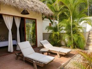 a patio with two chairs and a bed and palm trees at Casa Coconut in Puerto Escondido