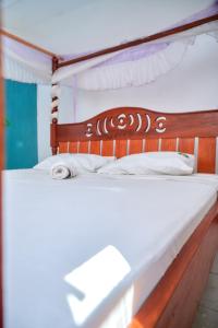 a bedroom with a wooden bed with white sheets at Tranquil Terrace Cottages Diani in Diani Beach +134 photos