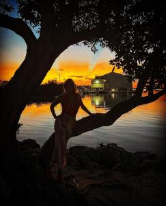 a woman sitting on a tree in front of the water at Crystal Waters - 2BR 2-5BA Coastal Villa in Duck Key