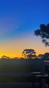 a sunset with trees in the background with two benches at Casa de Campo Bella Vista in Urupema