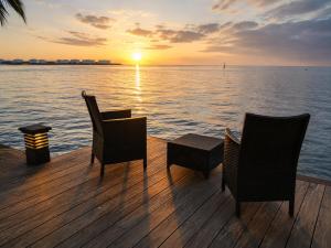 a wooden deck with chairs and a table and a sunset at Villa Manatini in Papeete