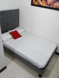 a white bed with a red pillow on it at Hospedajes Gold in Cali
