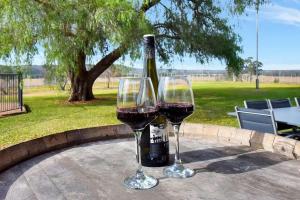 two glasses of wine on a table with a bottle of wine at Beggars Bridge Vineyard Homestead with pool and tennis in Rothbury