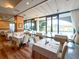 a restaurant with white tables and chairs and windows at Hotel LiVEMAX Nagasaki Airport in Omura