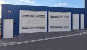 a row of three garage doors on a blue building at Cintra Home Araçariguama - Casa 04 in Araçariguama