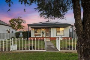 a white fence in front of a house with a tree at Sunday Valley in Cessnock